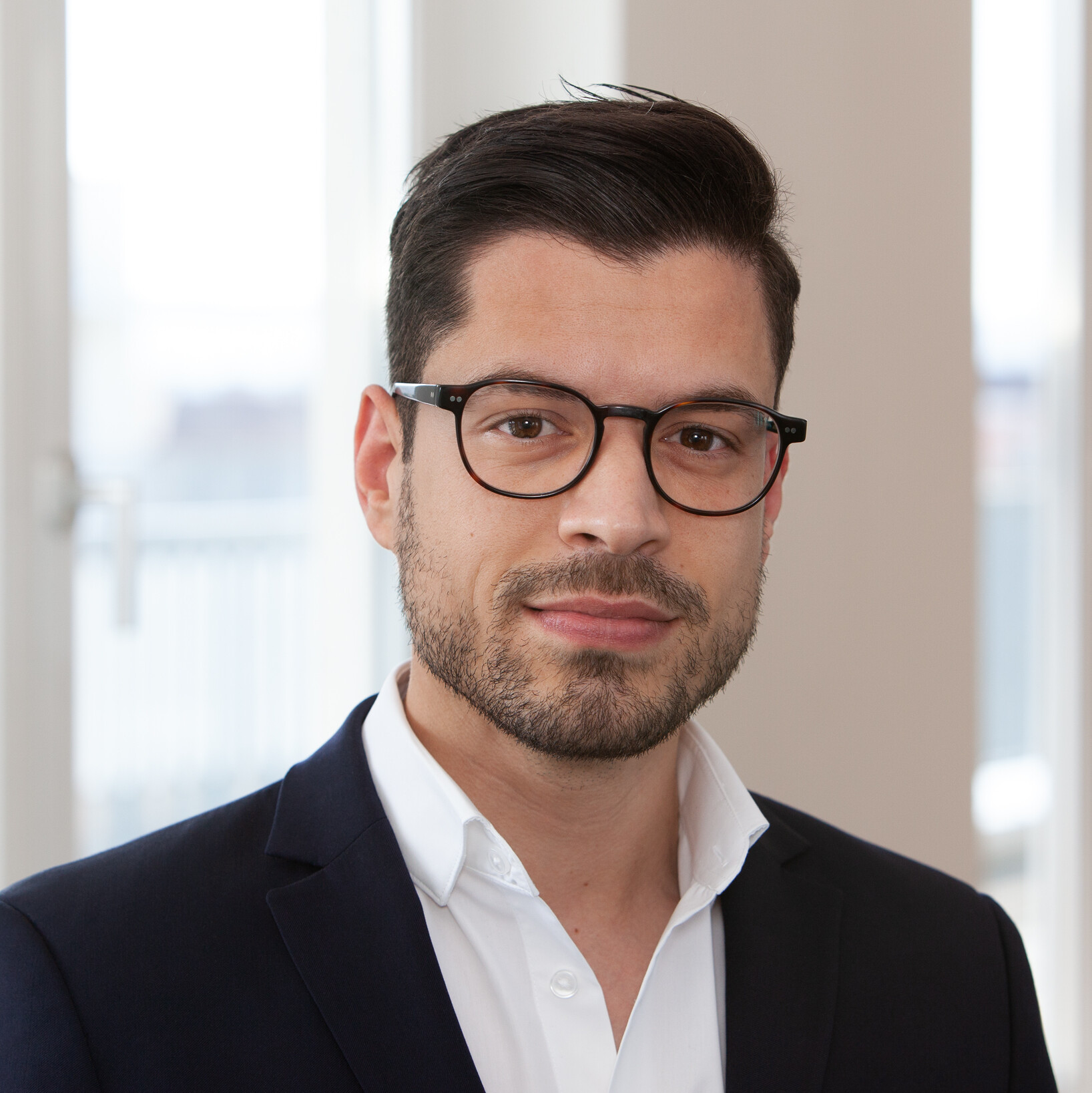 Ein Mann mit Brille und Anzug, der im Innenbereich fotografiert wurde.