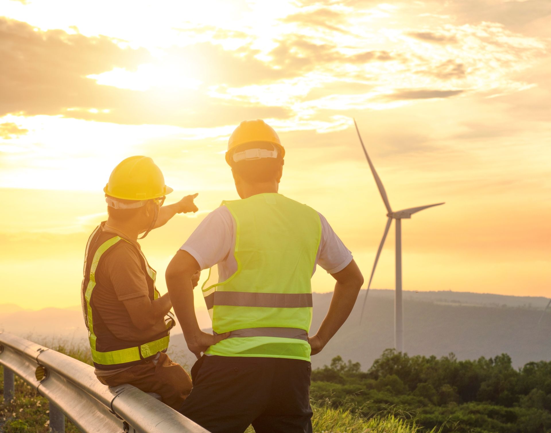 Zwei Männer in Sicherheitswesten und Helmen begutachten Windturbinen im Freien.